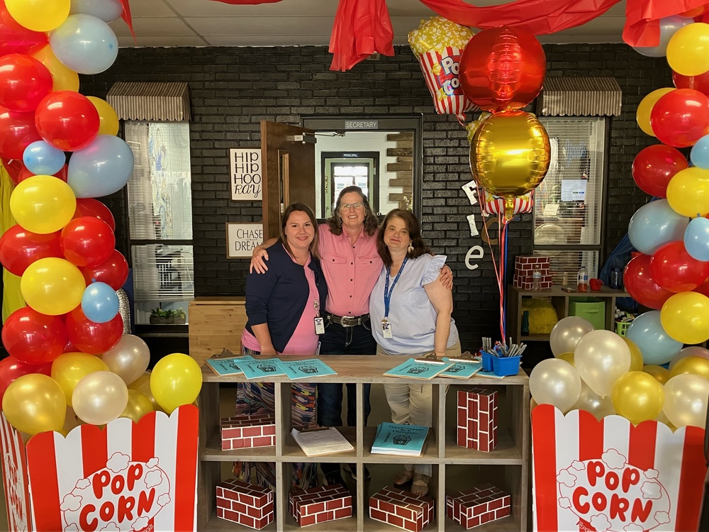 three women standing behind popcorn stand